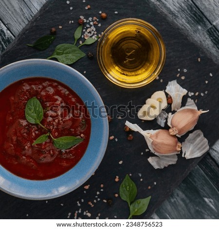 tomato sauce with black pepper and garlic, olive oil, and basil leaves on a dark backing in a blue plate