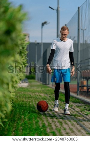 tall guy basketball player walks down the park path to the basketball court and drives the ball showing off his dribbling skills