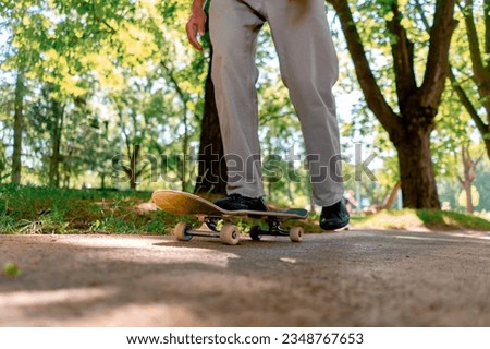 young guy skater rides skateboard on the path of the city park against the background of trees and sky close-up