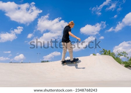A young guy skater does a stunt on the edge of a skatepool against a backdrop of sky and clouds at city skate park