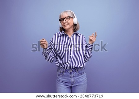 Energetic retired woman with gray hair masters headphone technique on a bright studio background