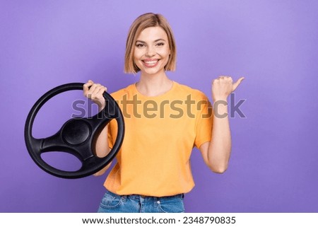 Photo of positive girl with bob hairstyle dressed yellow t-shirt hold steering wheel directing empty space isolated on violet background