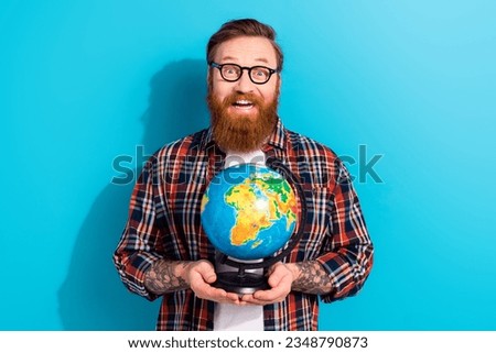 Photo of astonished funny young man wear glasses holding earth planet globus surprised discovering world isolated on blue color background