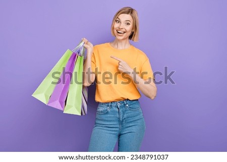 Portrait of ecstatic funny woman wear stylish t-shirt directing at shopping bags new clothes in hand isolated on purple background