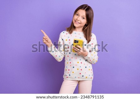 Portrait of charming cheerful schoolkid hold smart phone direct finger empty space promo isolated on purple color background