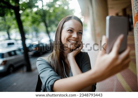 Young caucasian woman taking a picture with her smart phone while on a sidewalk in the city