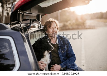 Middle aged caucasian man and his border collie dog sitting in a car trunk smiling