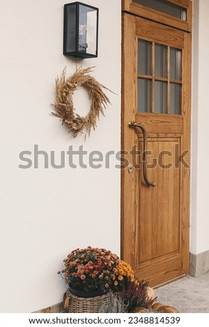 Autumn rustic wreath, pumpkins and flower pots at wooden front door. Stylish autumnal decor of farmhouse entrance or porch. Fall arrangement