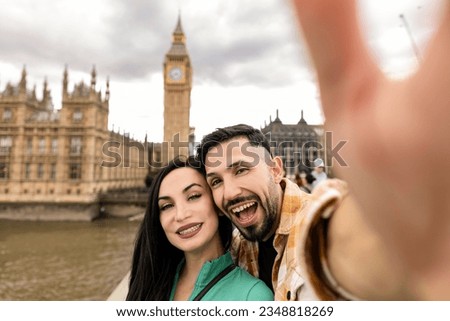 Smiling couple taking selfie portrait during travel in London, England - Young tourist taking vacation photo with iconic England landmark - Happy people wandering around Europe concept