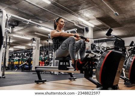 A muscular sportswoman in shape is doing workouts on a rowing machine. Royalty-Free Stock Photo #2348822597