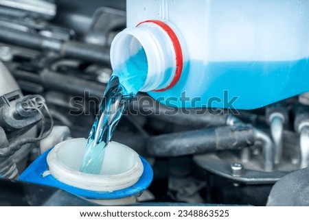Close-up of pouring coolant or windshield wiper fluid from bottle to reservoir. Checks levels and periodic maintenance of cars. Royalty-Free Stock Photo #2348863525