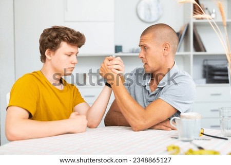 Happy smiling father and son arm wrestling at home. Fatherhood concept