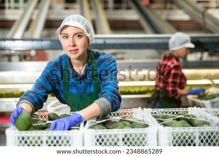 Positive woman in uniform during sorting at warehouse at avocado factory