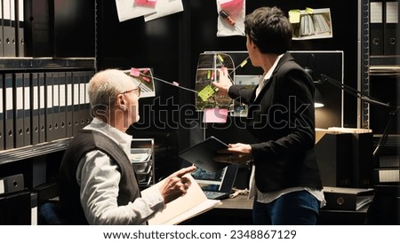 Police experts gathering clues for new criminal mistery in incident room. Detective coworking with law inspector to conduct investigation and solve organized crime case. Handheld shot. Royalty-Free Stock Photo #2348867129