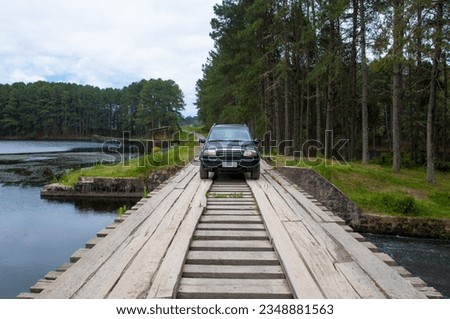 SUV car on a wooden bridge over a lake in the forest Royalty-Free Stock Photo #2348881563