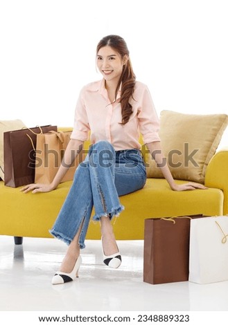 Portrait isolated cutout studio shot of Asian cheerful female client customer shopper in casual outfit sitting on cozy sofa take break buying stuff in paper shopping bags in store on white background. Royalty-Free Stock Photo #2348889323