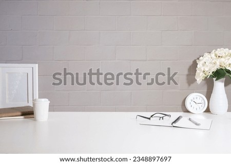 Home office interior. Picture frame, coffee cup, notebook and pencil holder on white table against brick wall. Copy space.