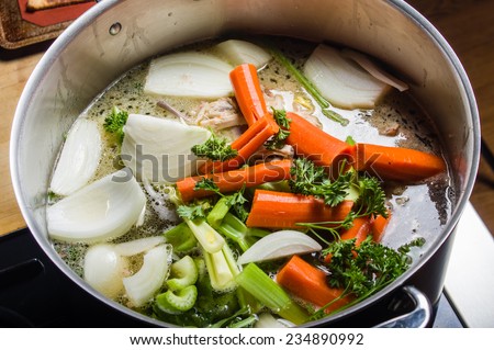 A large stock pot on a stove with vegetables cut for making soup