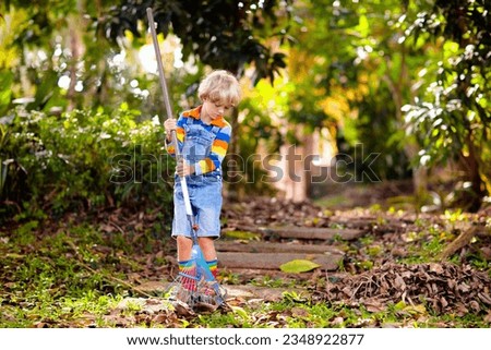 Child and rake in autumn garden. Kid raking leaves in fall. Gardening in foliage season. Little boy helping with backyard cleaning. Leaf pile on lawn. Kids help with chores. Children play outdoor. Royalty-Free Stock Photo #2348922877