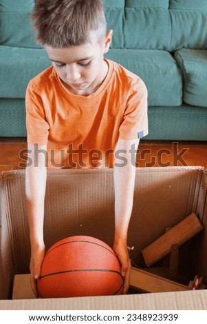 Boy in a house move picking up a basketball from a cardboard box