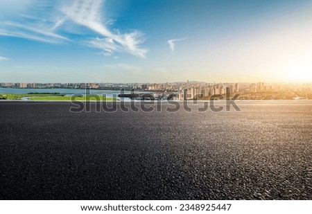 Asphalt road and urban skyline with lake at sunset