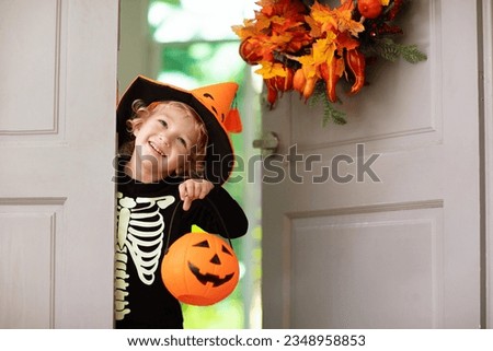 Kids trick or treat on Halloween night. Child at decorated house door with autumn leaf wreath and pumpkin lantern. Little boy in witch and skeleton costume and hat with candy bucket. Fall decoration. 
