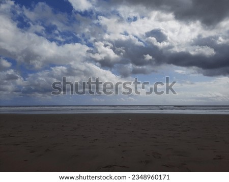 Sandy beach view with sky full of heavy white clouds.