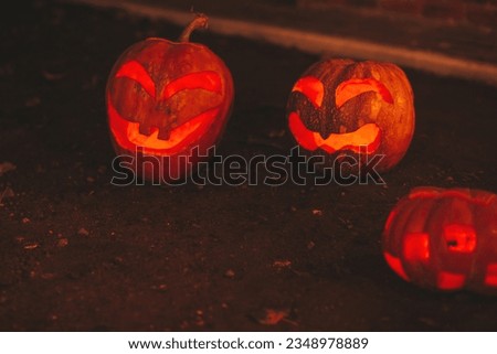 Scary jack lantern halloween pumpkins in darkness on ground among dry leaves at street. Hallows eve decoration funny glow pumpkin with candles on dark background in open air near house