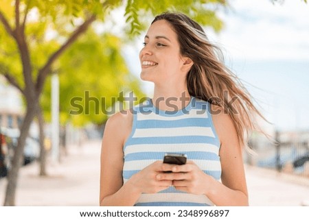Young pretty woman at outdoors using mobile phone and looking up