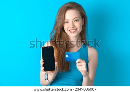Photo of adorable Young woman wearing blue T-shirt holding credit card and Smartphone. Reserved for online purchases