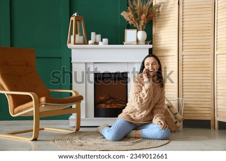 Young woman talking by mobile phone near fireplace at home