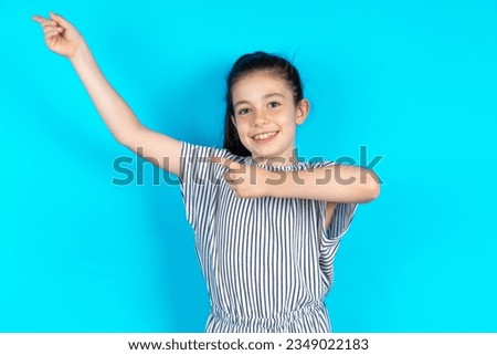 caucasian kid girl wearing striped dress indicating finger empty space showing best low prices, looking at the camera