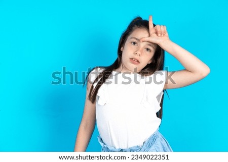 caucasian kid girl wearing white t-shirt making fun of people with fingers on forehead doing loser gesture mocking and insulting.