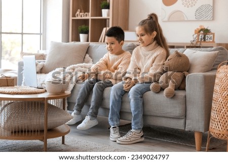 Cute little children in knitted sweaters watching cartoons at home