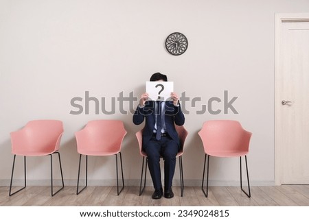 Male applicant holding paper sheet with question mark in room
