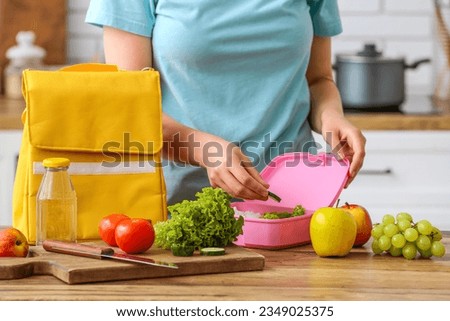Woman packing fresh meal into lunch box in kitchen Royalty-Free Stock Photo #2349025375