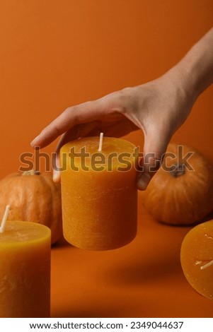 Candle in female hand and pumpkins on orange background