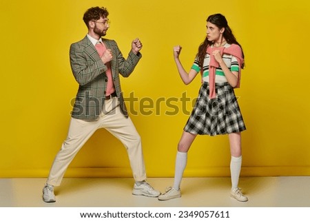 fight, man against woman, young man and woman with clenched fists, opponents, yellow backdrop Royalty-Free Stock Photo #2349057611