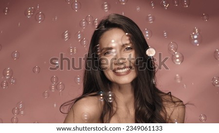 Joyful, playful woman surrounded by soap bubbles. A seminude woman with flowing hair in the studio on a pink background. Lightness, childhood. Royalty-Free Stock Photo #2349061133