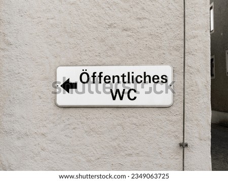 Öffentliches WC (public toilet) sign with a directional arrow on a house wall. The information is in close up and is guiding to a restroom in Germany.