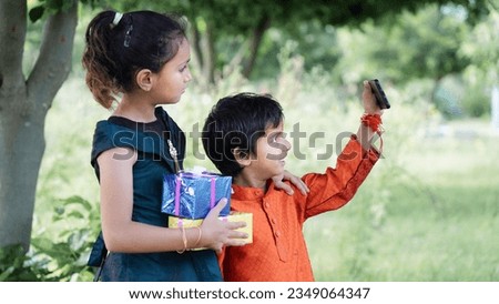 Indian good looking little brother and sister celebrating Raksha Bandhan festival or on Bhai dooj with gifts or taking selfie pictures - Season's Greeting Card