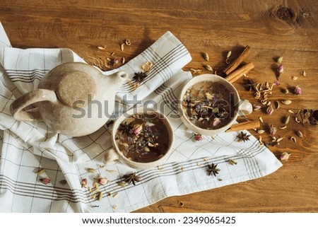 Herbal tea,cinnamon, dried rose,cardamom,orange blossom,and star anise are the ingredients in this nutritious tea next to the teapot, and cups are on a wooden background Delicious organic brewed drink