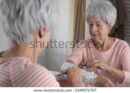 Senior woman shaving her hairy forearms 