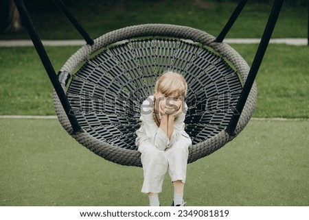 Joyful blonde-haired girl gleefully swings under the golden sun, her laughter echoing in the air as she soars higher with every joyful push, embracing the simple delight of carefree moments.