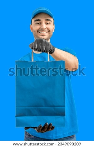 Delivery man with paper bag. Courier in uniform cap and t-shirt, gloves service fast delivering orders. Young guy holding a paper package. Character on isolated background for mockup design Royalty-Free Stock Photo #2349090209