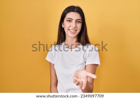 Young beautiful woman standing over yellow background smiling cheerful offering palm hand giving assistance and acceptance. 