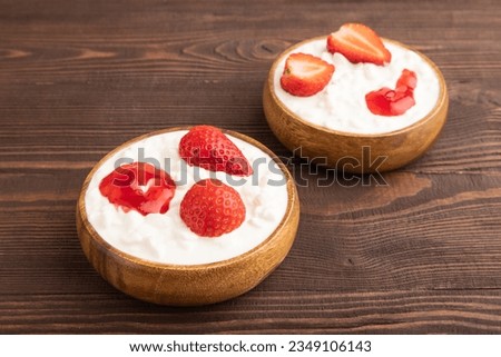 Grained cottage cheese with strawberry jam on brown wooden background. side view, close up.