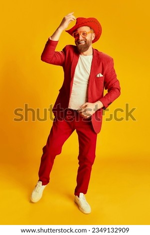 Fashionable man, hipster wearing bright red costume and cowboy hat posing over yellow background. Concept of style , fashion, happy mood, positive emotions and facial expression