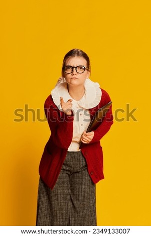 One young girl wearing old-fashioned outfit posing over yellow background. Retro vintage fashion, business, education and emotions. Copy space for ad