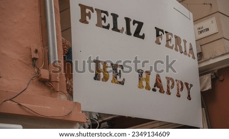 Low angle view of white poster with feliz feria be happy text carving hanging outside building wall in old town at Andalusia, Spain
